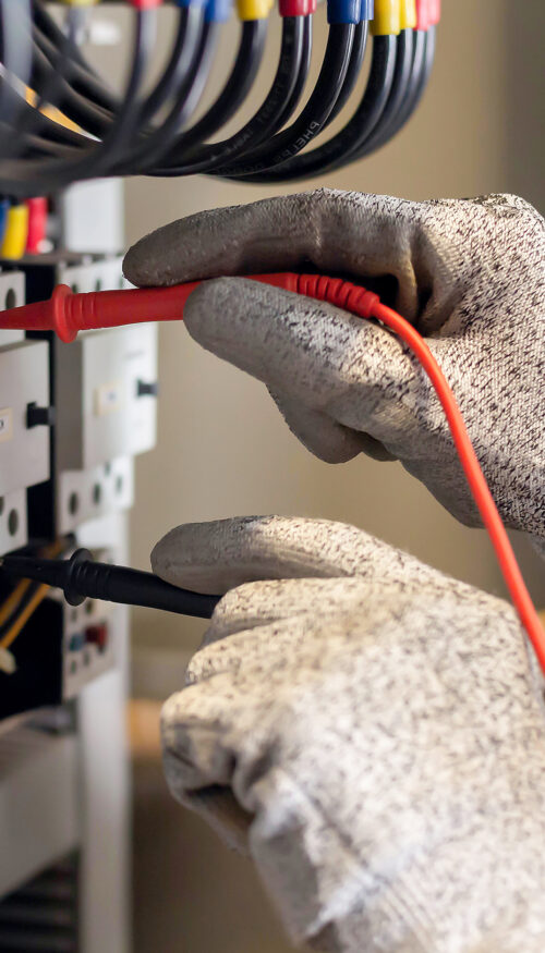 Electrician engineer uses a multimeter to test the electrical installation and power line current in an electrical system control cabinet.